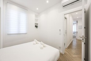 A modern bedroom with a large bed, a small window, and an air conditioning unit.