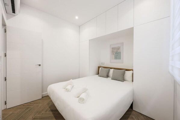 A bedroom with a bed, a door, and a wall-mounted air conditioning unit.