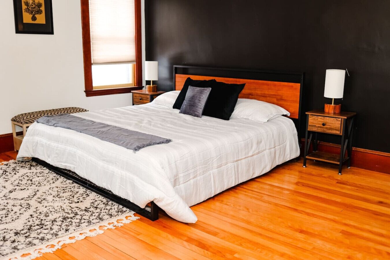 Un dormitorio con cama, mesitas de noche, una ventana y una lámpara fijada a la pared.