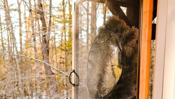 Une porte en bois avec un panneau de verre, donnant sur un espace extérieur enneigé bordé d’arbres.
