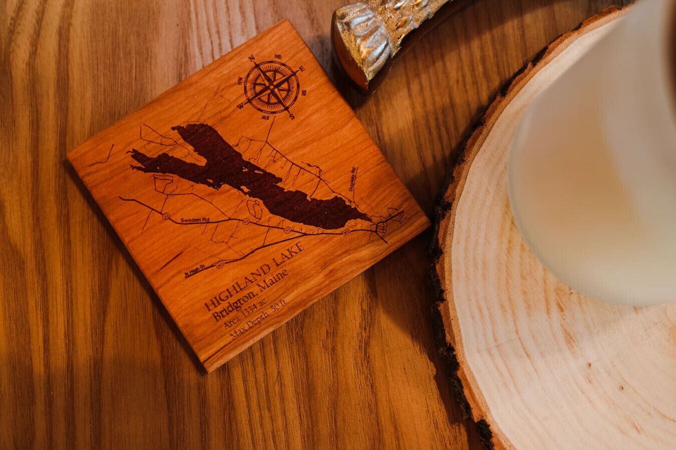 Un posavasos de madera con un mapa del Lago Highland, Maine, que incluye una rosa de los vientos y la silueta de un bote.