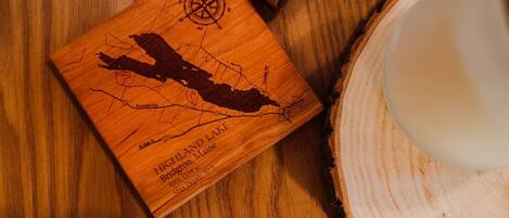 Un posavasos de madera con un mapa del Lago Highland, Maine, que incluye una rosa de los vientos y la silueta de un bote.
