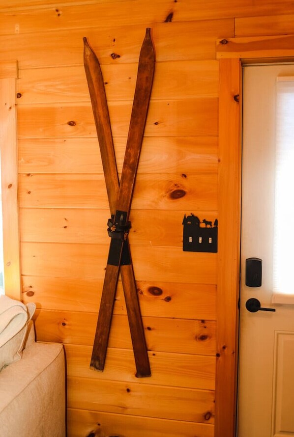 A wooden wall with a pair of skis crossed over each other, a door with a black handle, and a small black sign with a silhouette of a house and a horse.