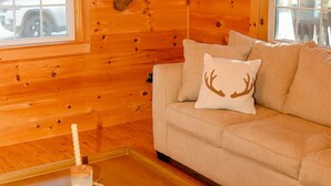 L’intérieur d’un chalet accueillant, avec un plancher en bois, un canapé agrémenté d’un coussin en forme de cerf et une paire de bottes accrochées au mur.