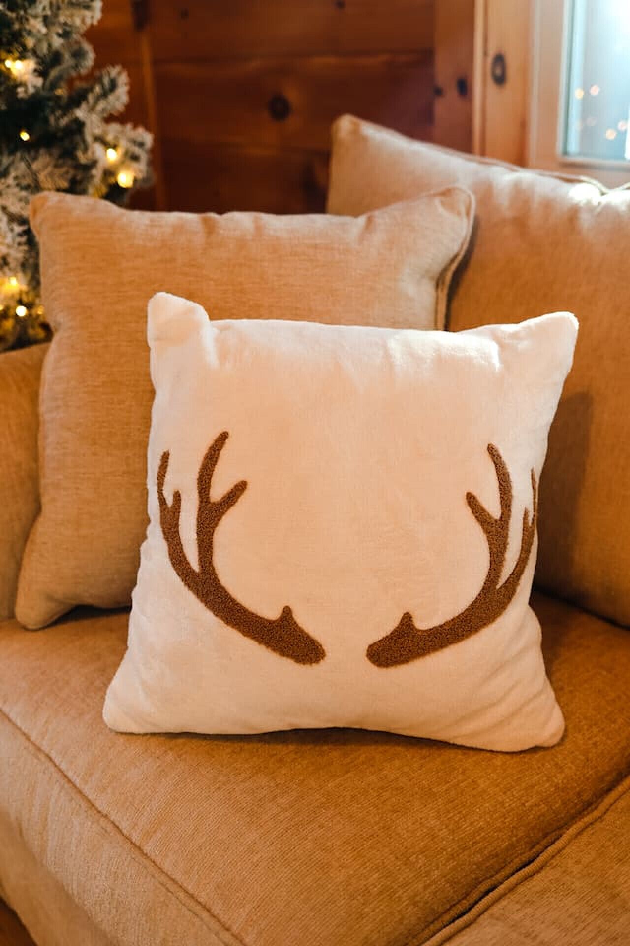 A beige sofa with a white pillow featuring a deer antler design.