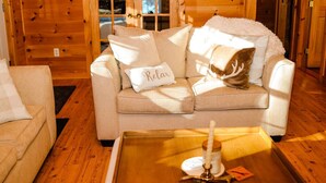 L’intérieur d’un chalet accueillant, avec un canapé beige, une petite table sur laquelle est posée une bougie, et une porte en bois à l’arrière-plan.