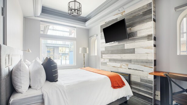 A hotel room with a large bed, a mounted TV, and a view of the street through the window. - La TUMU (Toronto)