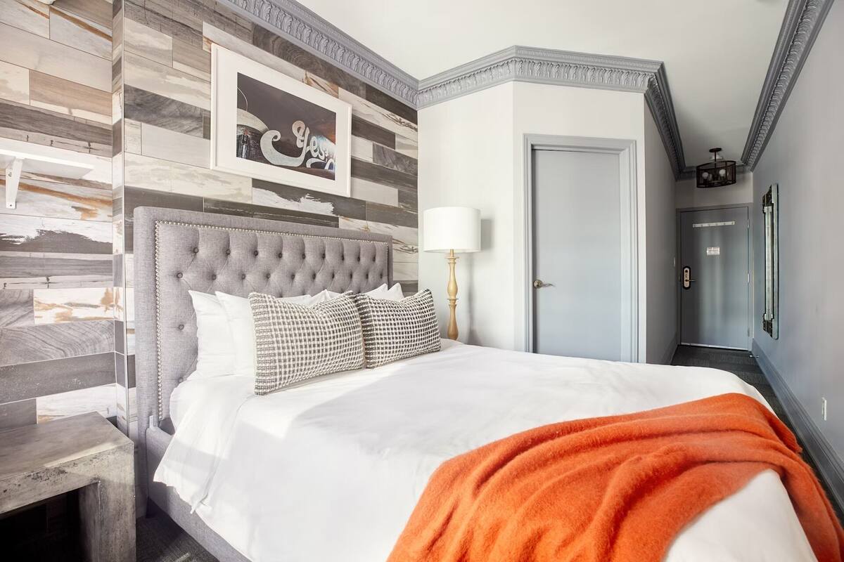 A hotel room with a bed, a nightstand, a lamp, and a door.