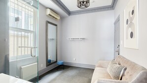 A modern bathroom with a glass shower enclosure, a white bathtub, and a beige sofa with a patterned pillow. - La TUMU (Toronto)