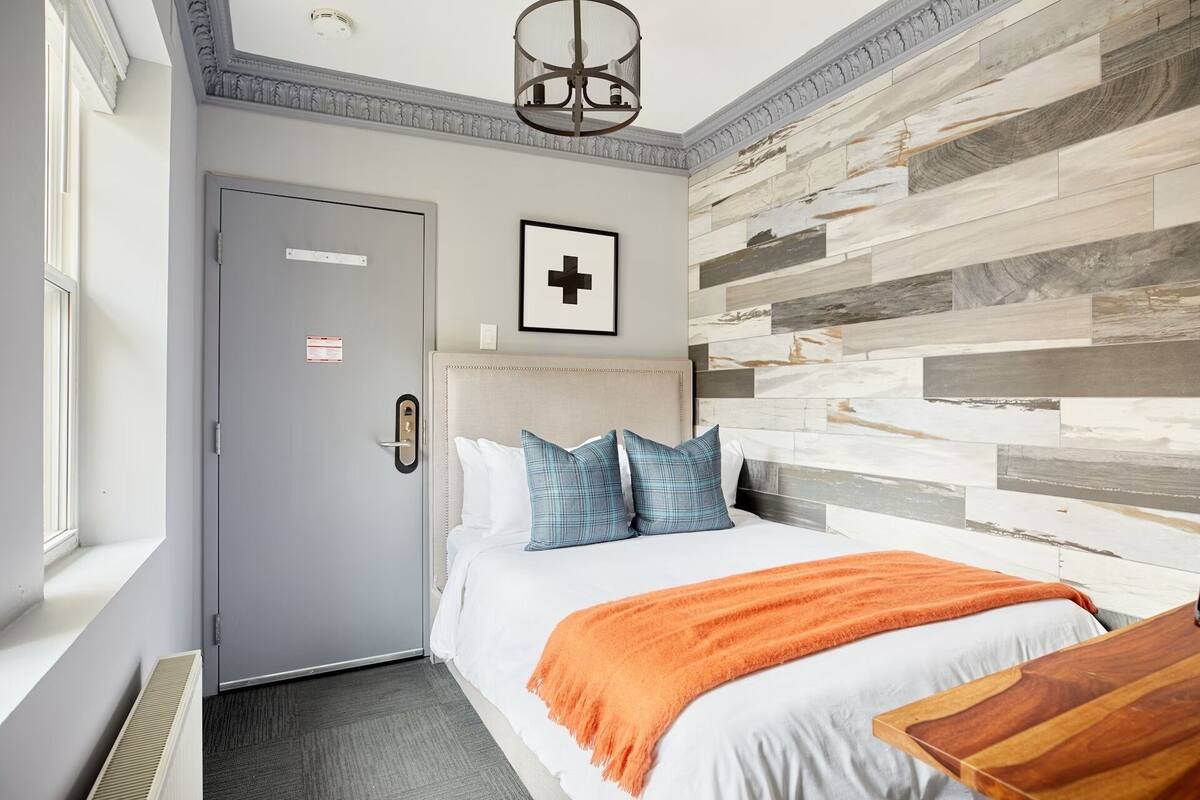 A hotel room with a bed, a wooden accent wall, a door with a sign, and a window.