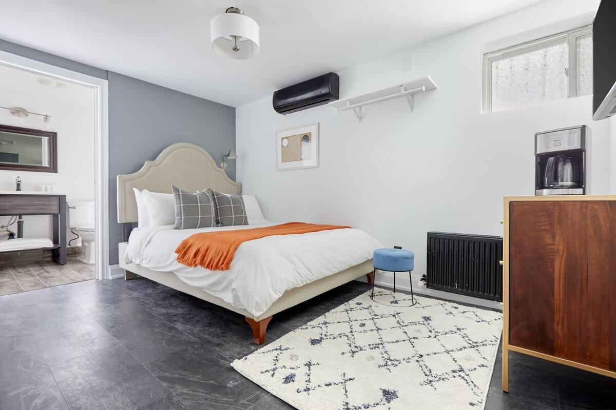 A modern bedroom with a bed, bedside table, radiator, and a view of the bathroom.