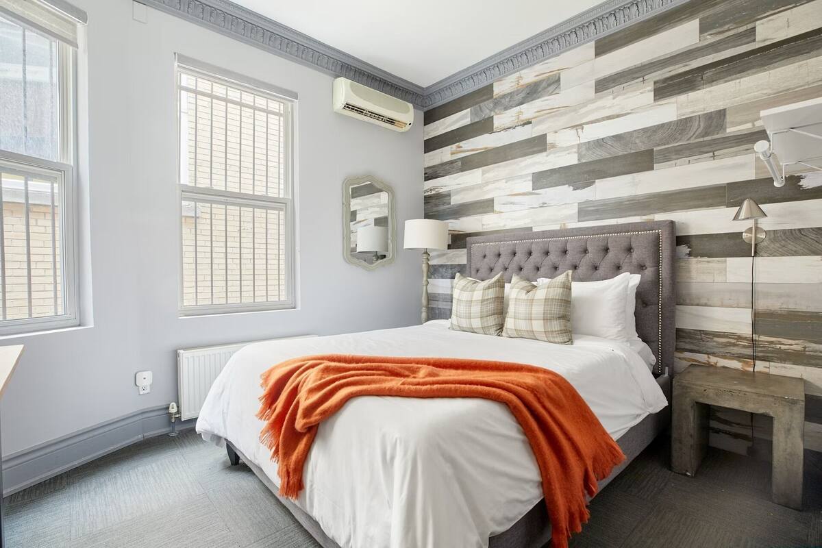A bedroom with a bed, a nightstand, a lamp, a mirror, and a window.