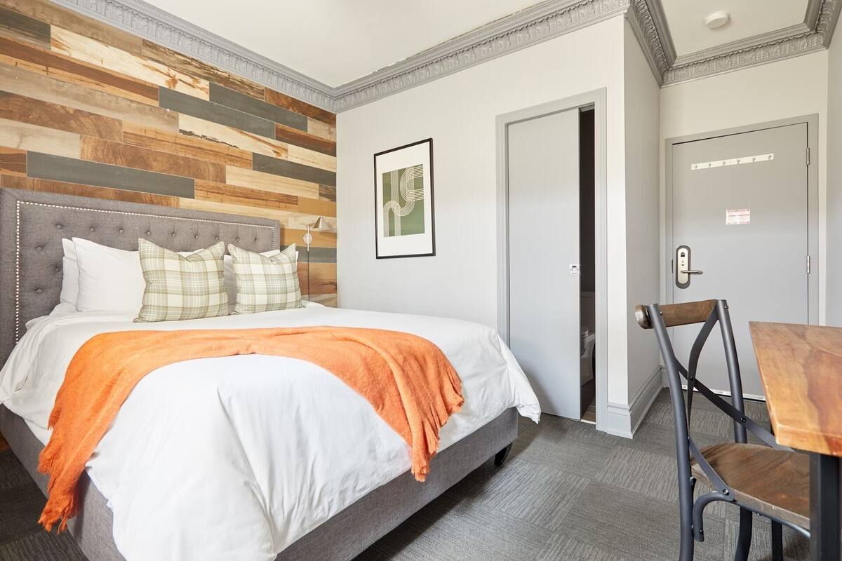A hotel room with a bed, a desk, and a door.