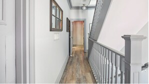 A hallway with a wooden floor, white walls, and a staircase with a gray railing. - La TUMU (Toronto)