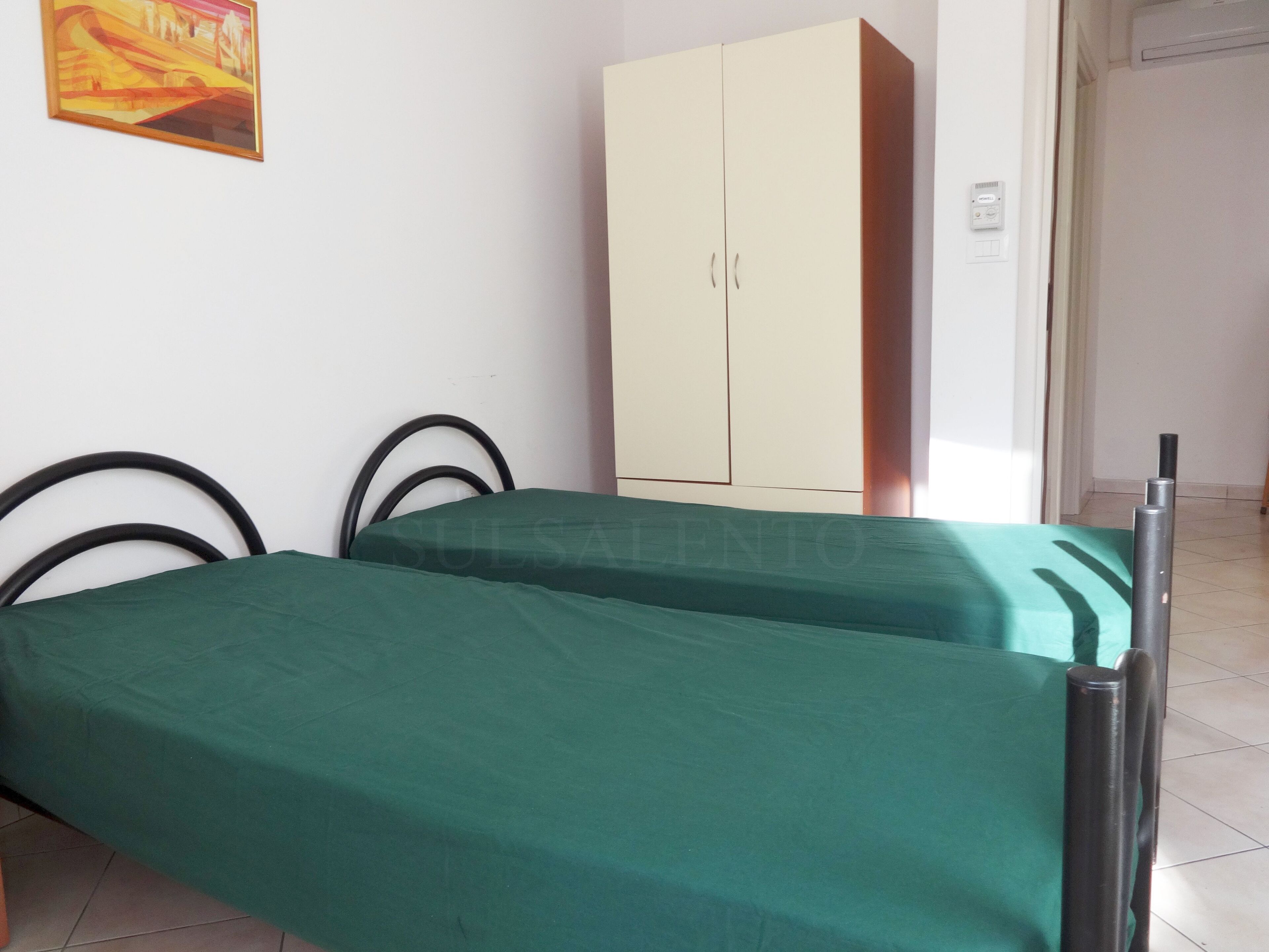 Een kamer met twee bedden, een garderobe en een schilderij aan de muur.