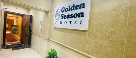 Une enseigne indiquant l’hôtel Golden Season, placée dans un couloir aux murs carrelés, avec une plante en pot.