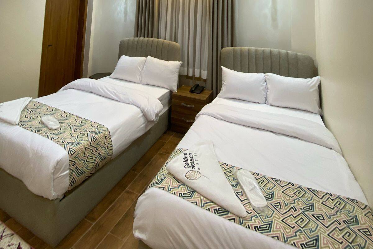 A hotel room with two beds, a wooden door, a ceiling light, and an air conditioning unit.