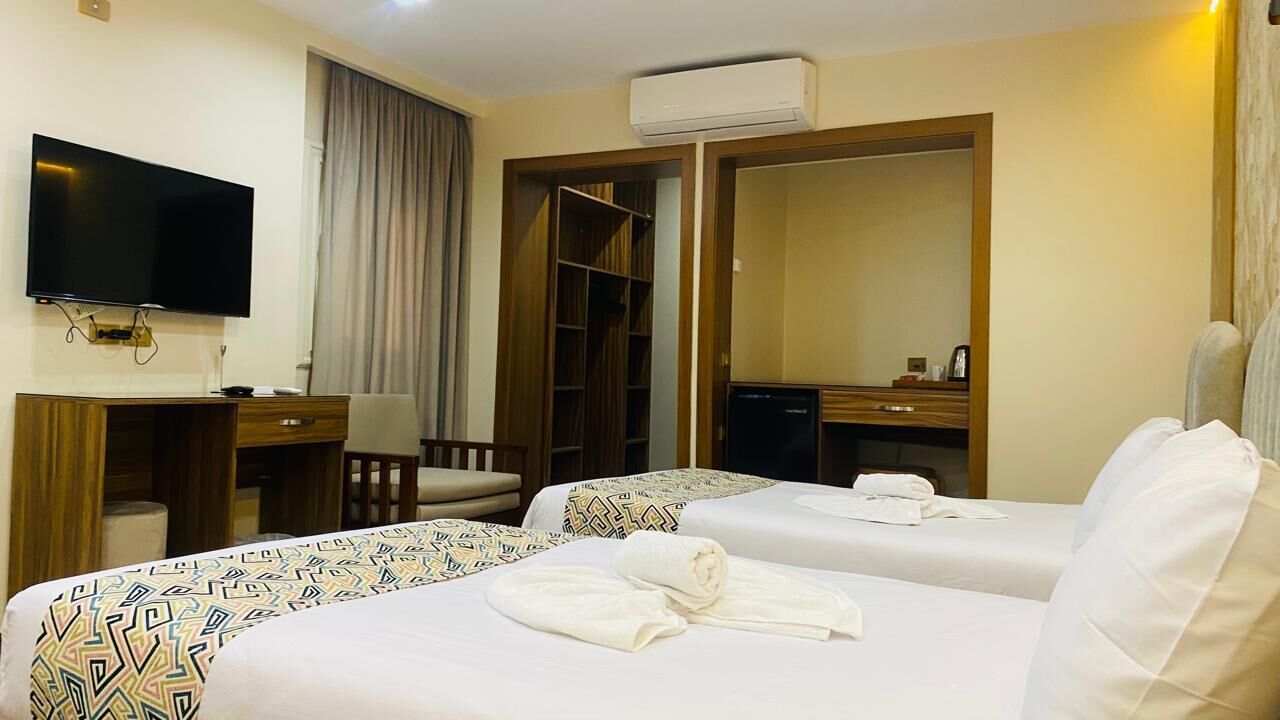 Een hotelkamer met twee bedden, een televisie, een bureau, een stoel, een kledingkast en een airconditioningsysteem.
