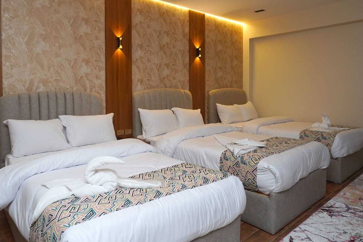 A hotel room with three beds, a marble-patterned wall, and wall-mounted lighting.