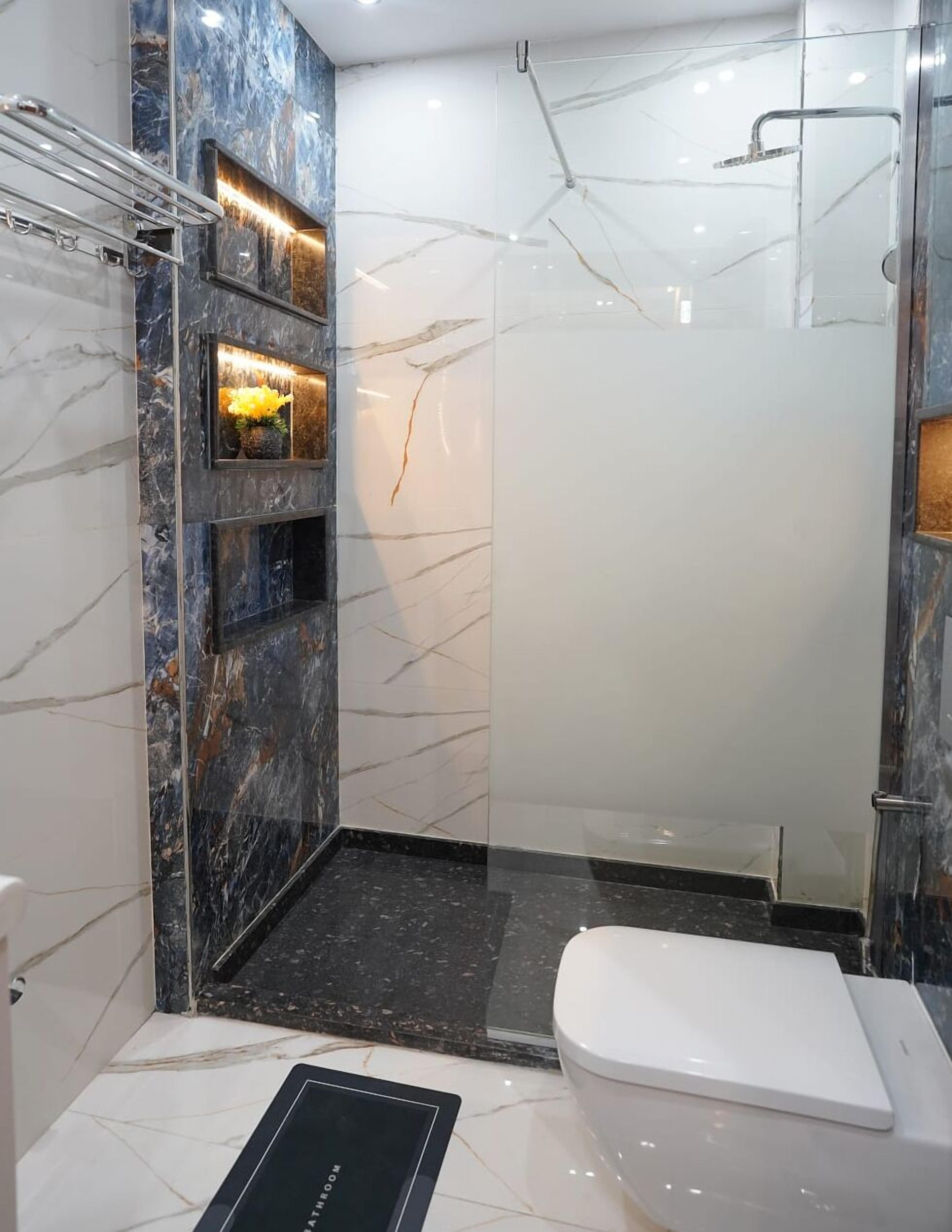 A modern bathroom with a glass shower enclosure, marble walls, and a white toilet.