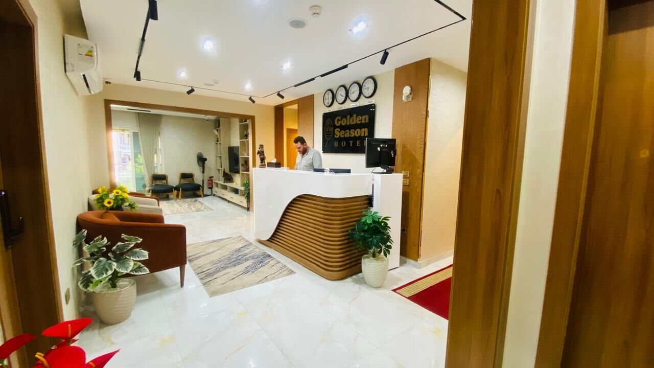 Zona de recepción de hotel con diseño moderno, que incluye un mostrador de recepción, un área de estar y un pasillo visible que conduce a otras habitaciones.