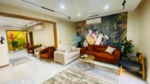 A modern living room with a beige sofa, a red sofa, and a glass coffee table. There is a large mural on the wall and a small table with flowers. - Golden Season Hotel  (Cairo)