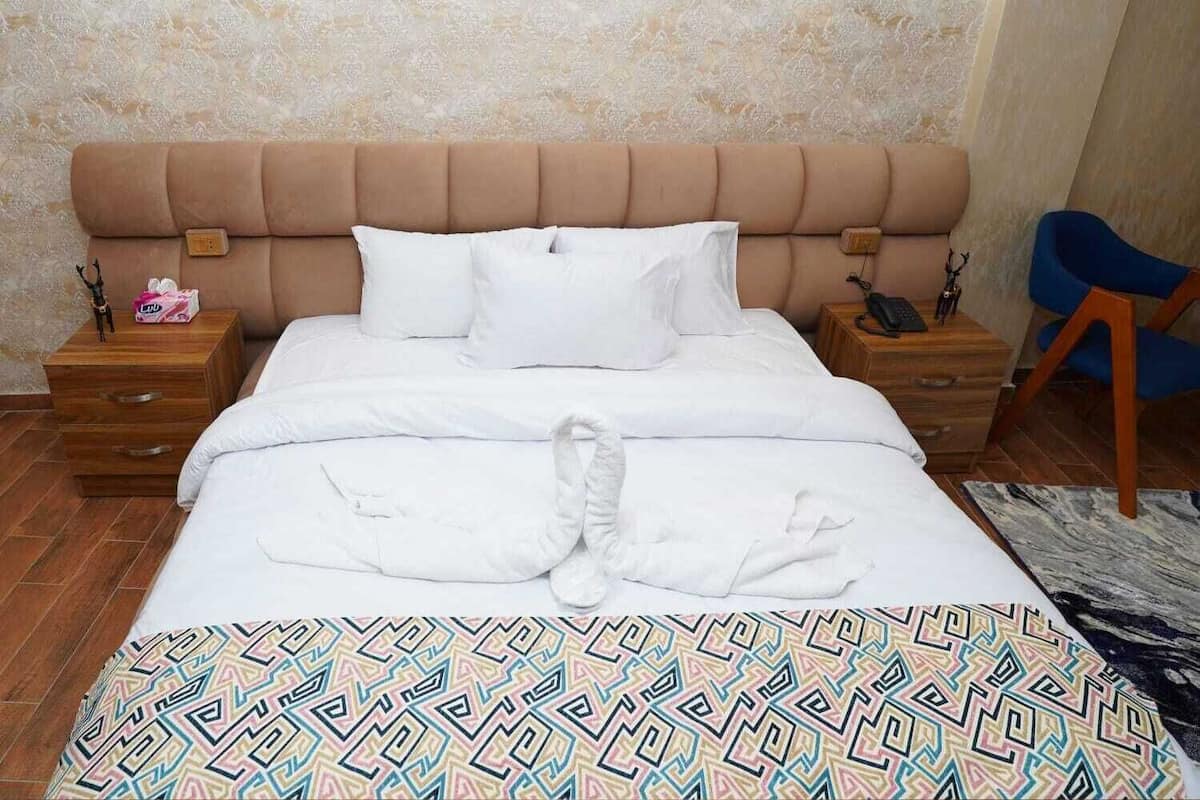 A hotel room with a large bed, two bedside tables, a headboard, and a patterned rug.