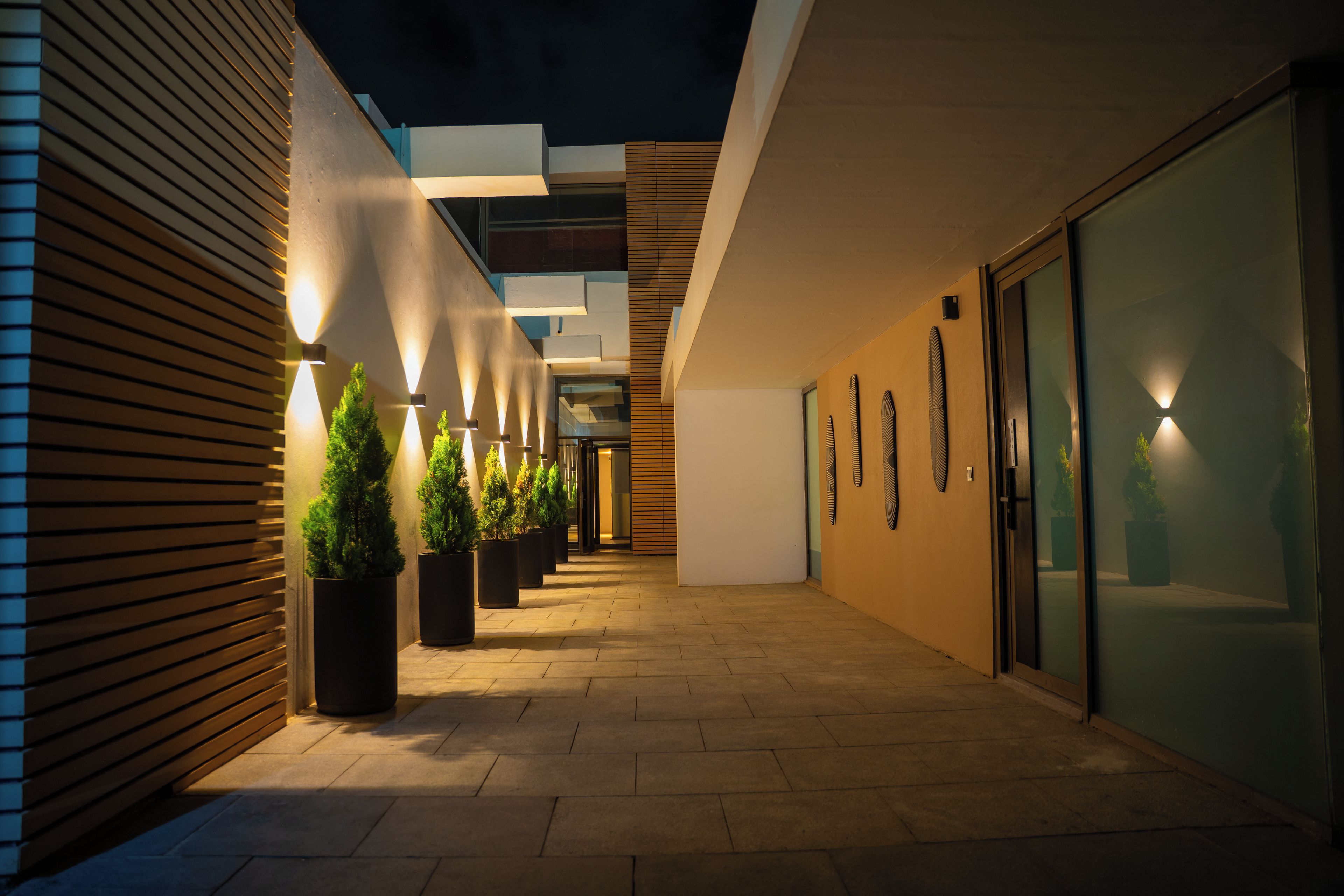 A corridor with potted plants and wall-mounted lights.