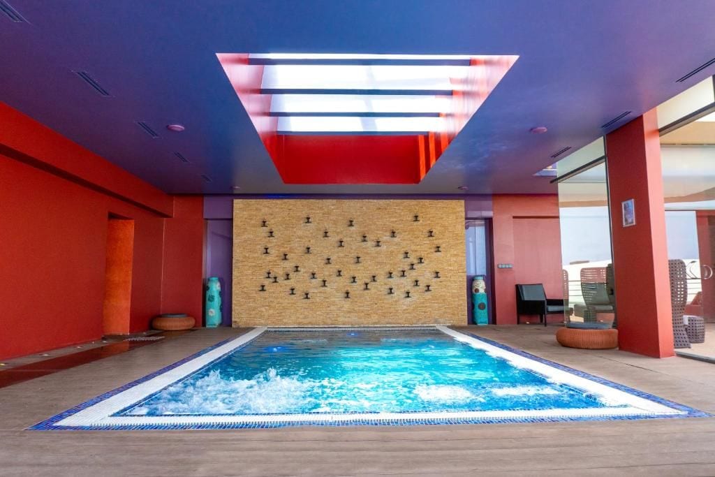 A swimming pool with a tiled border, a wooden wall with a pattern of black symbols, and a red ceiling with a skylight.