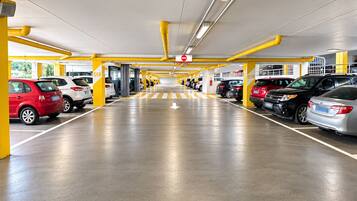 Un parking à étages avec plusieurs rangées de voitures garées, des piliers de soutien jaunes et des flèches directionnelles peintes sur le sol.