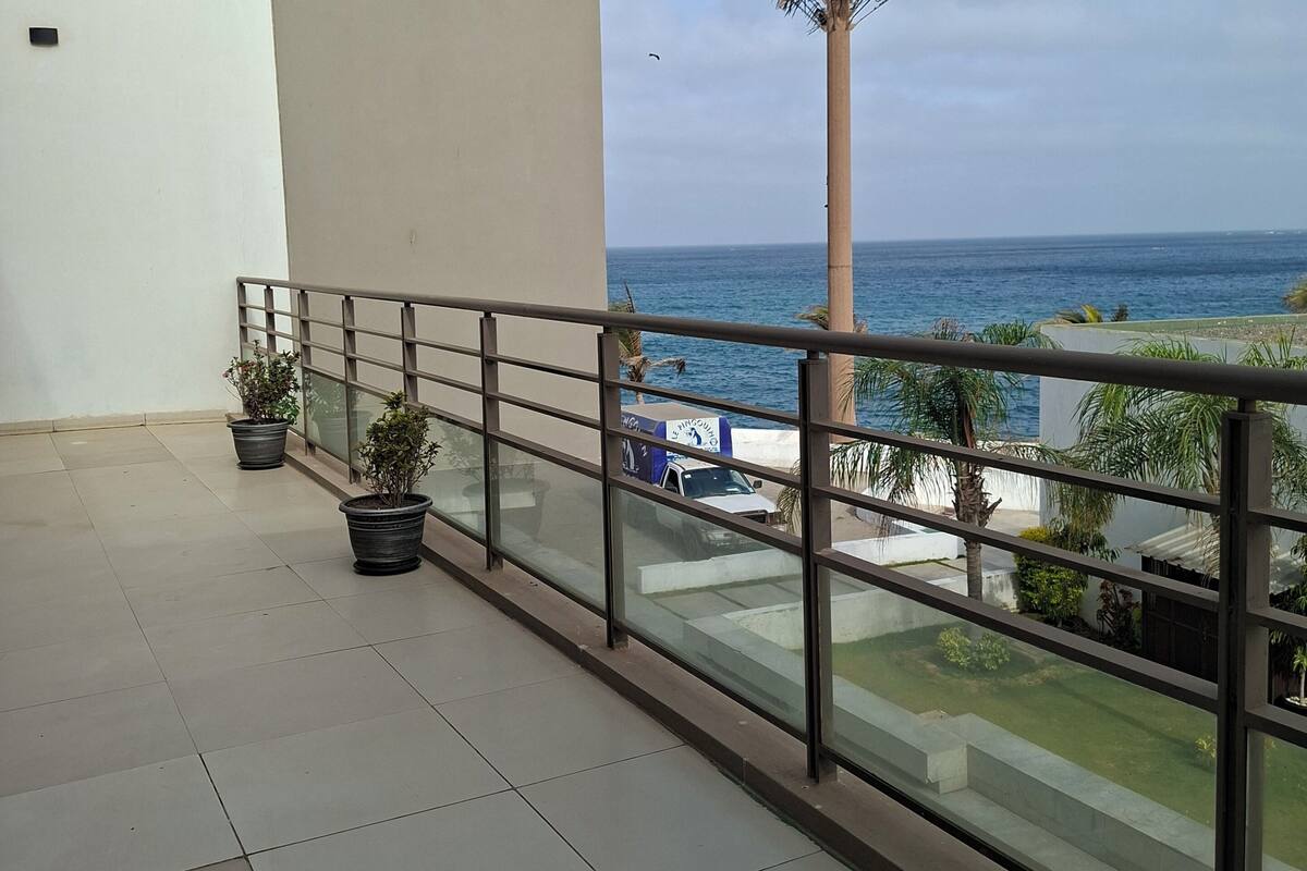 A balcony with a view of the sea, potted plants, and a utility pole.