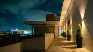 Un edificio moderno con un espacio exterior cubierto, plantas en macetas y un camino que lleva a una puerta.