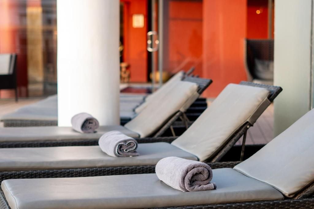 A row of sun loungers with towels, a glass partition, and a red wall in the background.