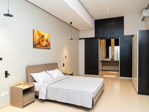 Ein modernes Hotelzimmer mit Bett, Nachttischen, einem Gemälde, einem Kleiderschrank und einem durch eine geöffnete Tür einsehbaren Badezimmer.