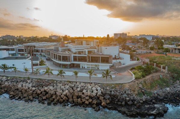 A coastal hotel with a modern design, featuring a prominent curved structure, a rocky shoreline, and a view of the sea. - La Résidence Sea Plaza (Dakar)