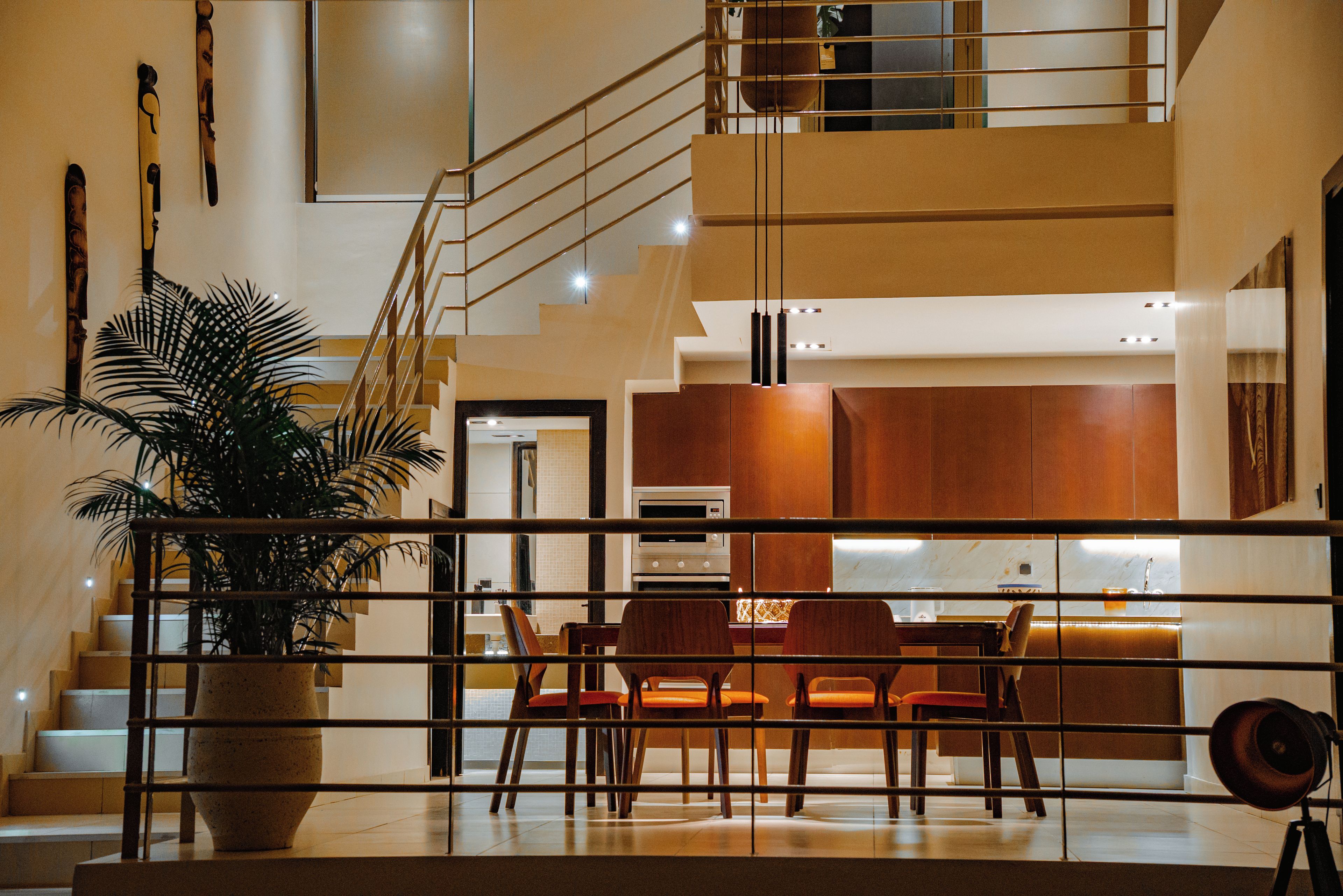 A modern interior with a staircase, a dining area with wooden chairs, and a large potted plant.