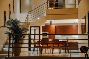 A modern interior with a staircase, a dining area with wooden chairs, and a large potted plant. - La Résidence Sea Plaza (Dakar)