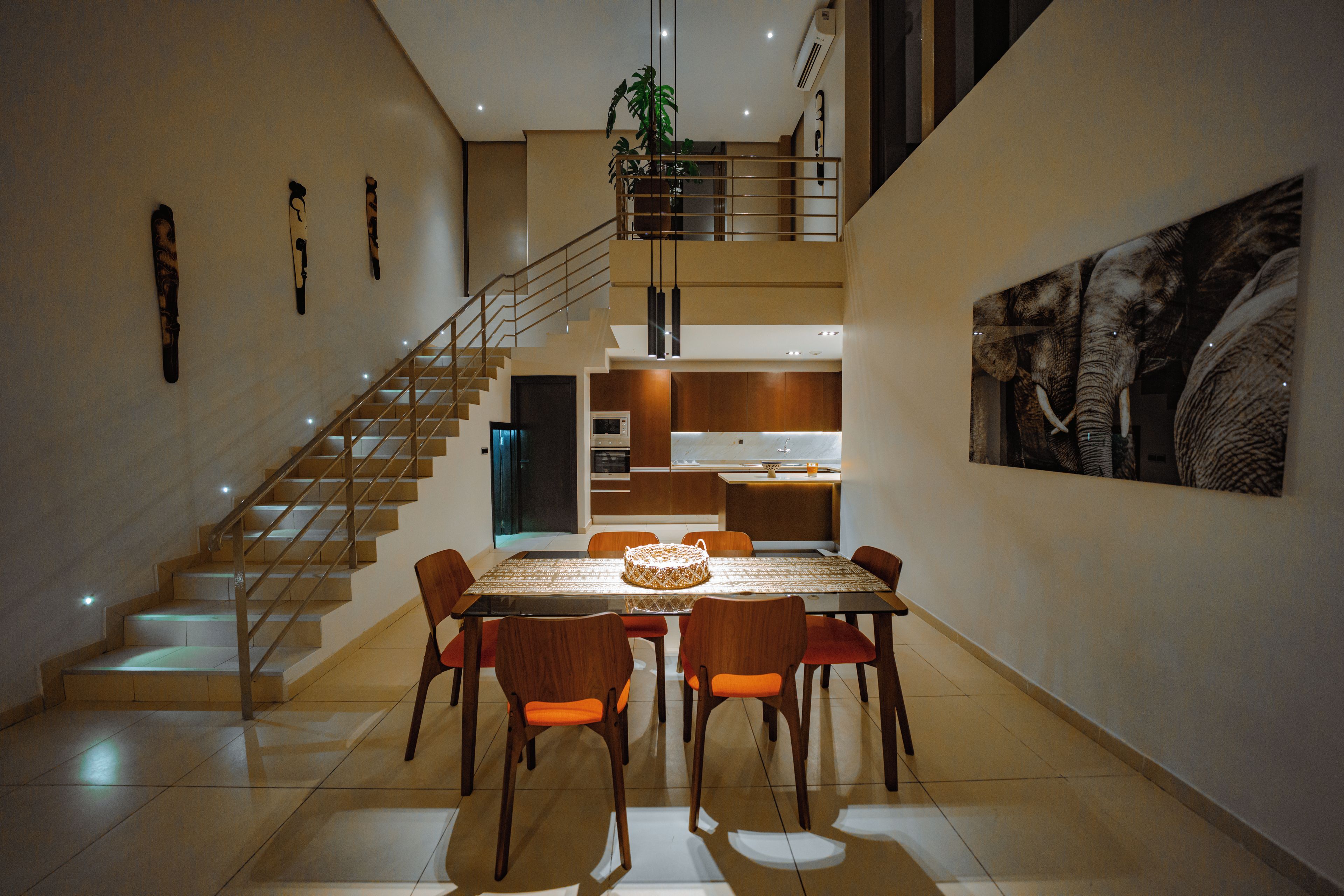 Un comedor amplio con techo alto, una escalera que conduce a un nivel superior y una gran obra de arte colgada en la pared.
