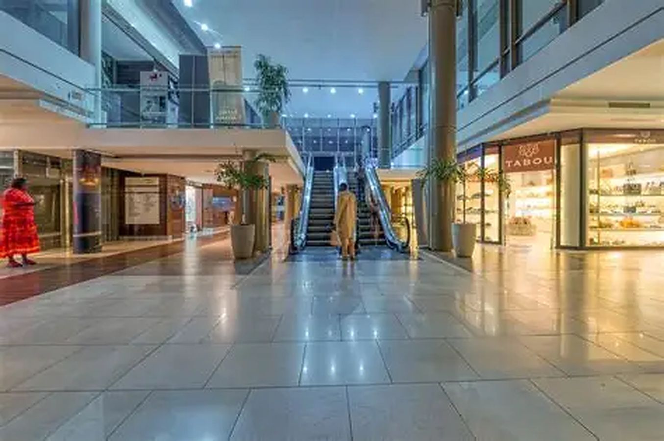 Un vaste espace intérieur doté d’un escalier central, de plantes en pot et d’un magasin appelé « TABOU » situé sur la droite.