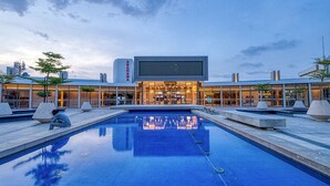 A modern building with a large pool in the foreground, a cinema sign above the entrance, and a clear sky in the background. - La Résidence Sea Plaza (Dakar)