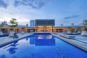 A modern building with a large pool in the foreground, a cinema sign above the entrance, and a clear sky in the background. - La Résidence Sea Plaza (Dakar)