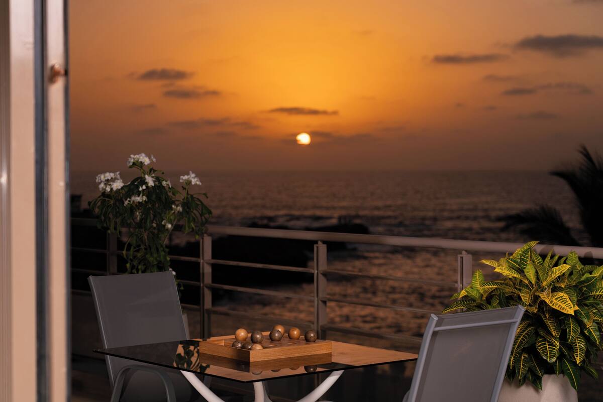 A table with a chessboard and a plant, overlooking a beach at sunset.