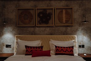 Een bed met een gewatteerd hoofdbord, twee witte kussens en twee kussens met een patroon. Daarboven hangen drie kunstwerken in lijsten.