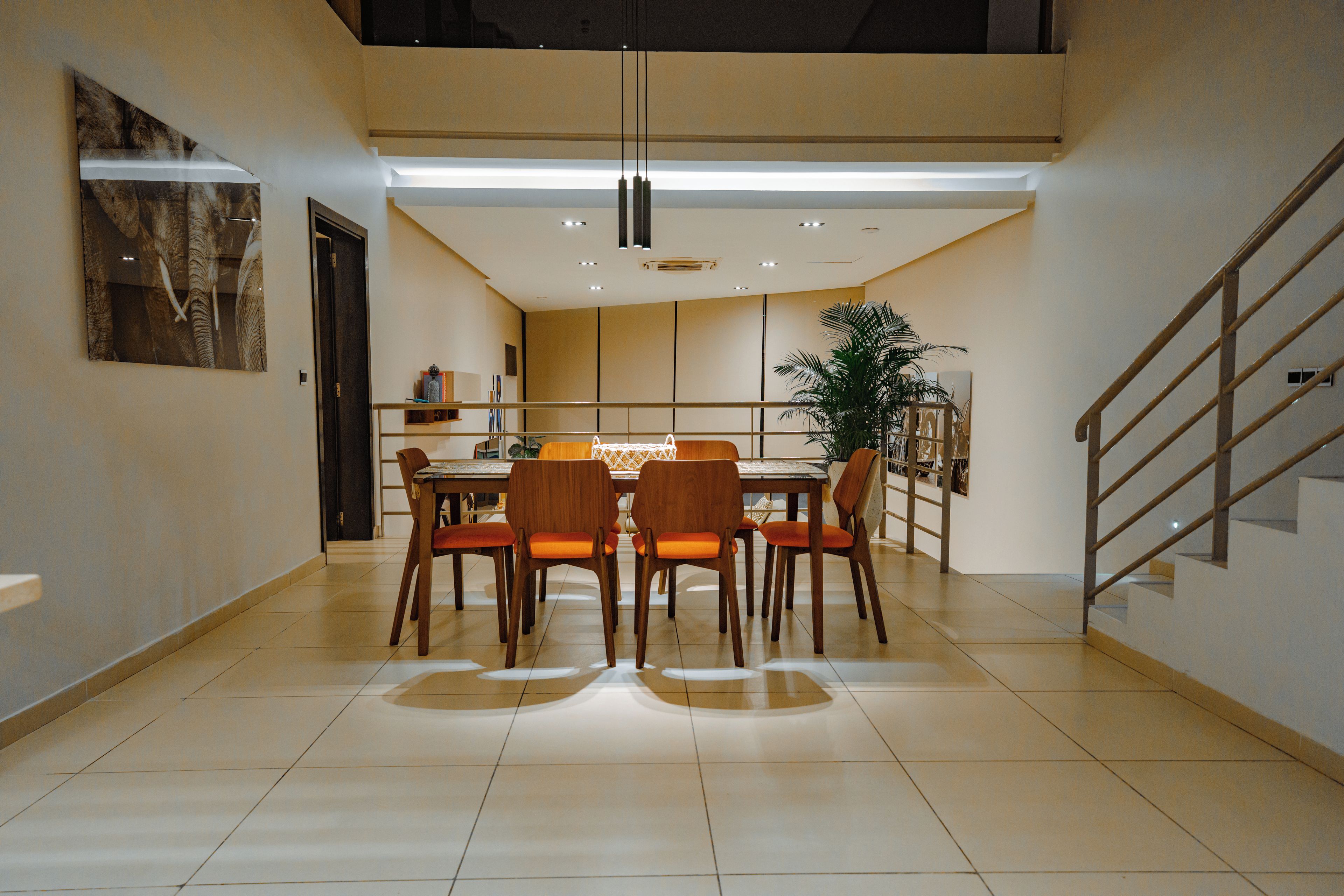 Un área de comedor moderna con techo alto, iluminación empotrada y una escalera a la derecha.