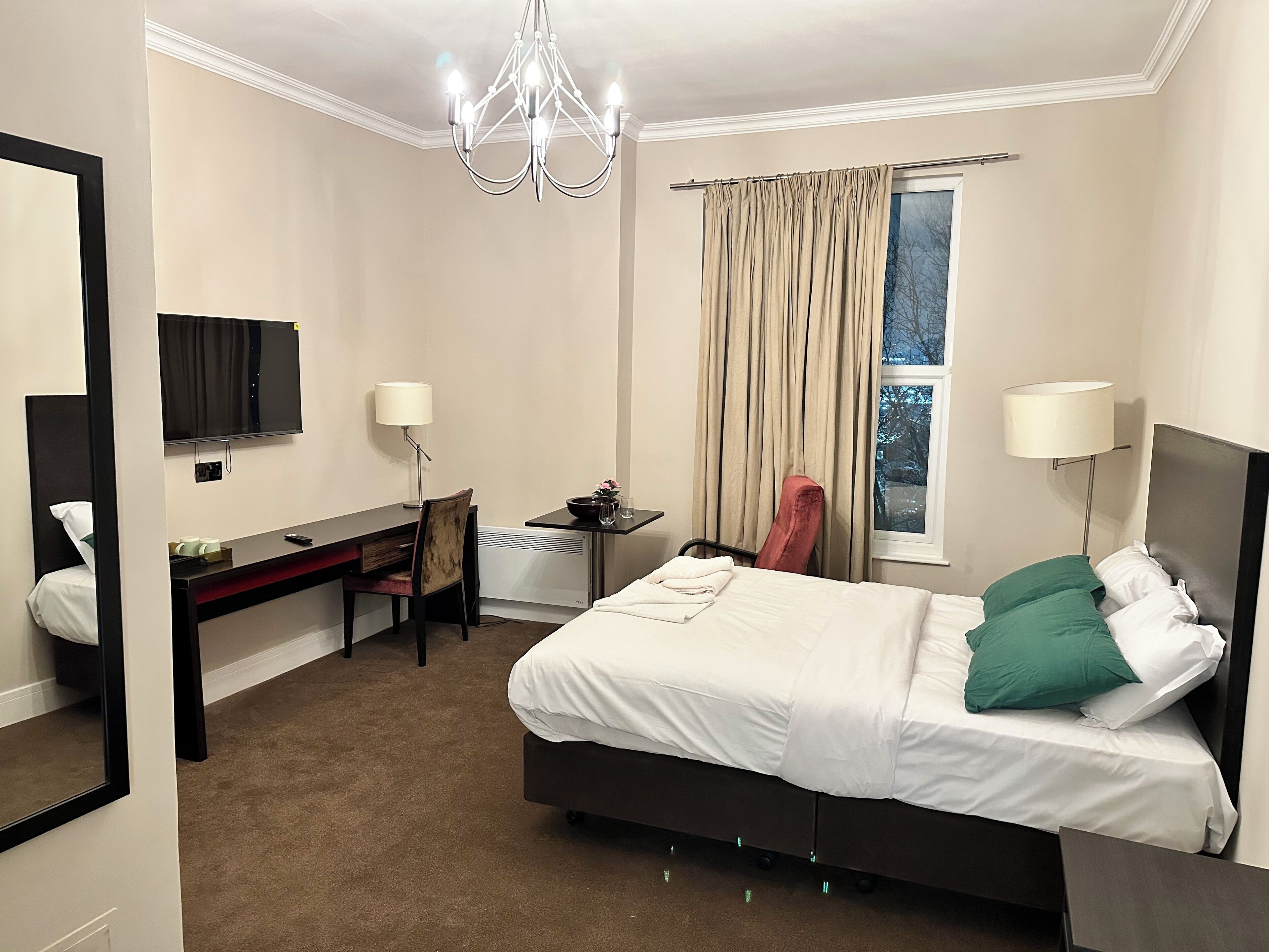 A hotel room with a bed, a desk, a chair, a TV, and a window with curtains.