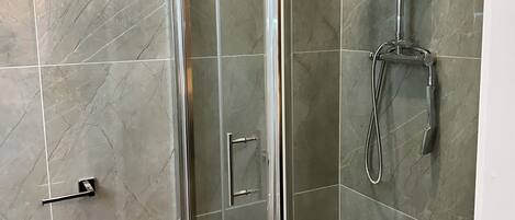 A glass-enclosed shower with a handheld showerhead and a wall-mounted faucet.