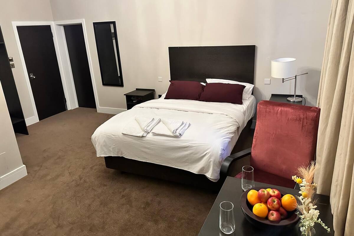 Ein Hotelzimmer mit einem Bett, Nachttischen, einem Schreibtisch mit einer Fruchtschale und einem roten Sessel.