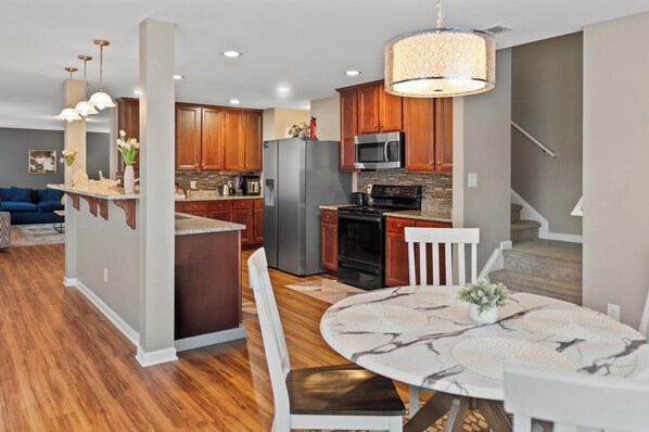 A modern kitchen with wooden cabinets, stainless steel appliances, and a dining area with a marble table.