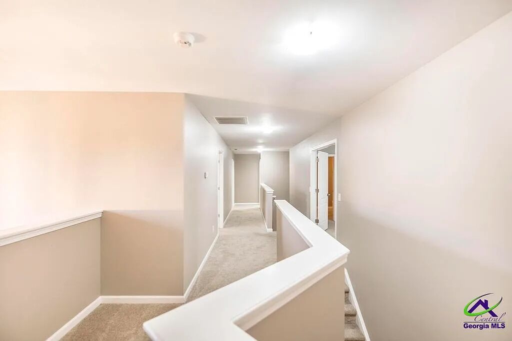 A narrow, carpeted hallway with white walls and a white railing.