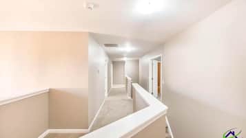 A narrow, carpeted hallway with white walls and a white railing.
